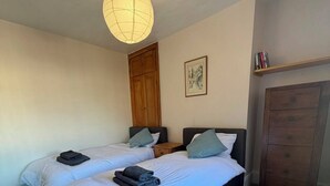 A bedroom with two beds, a wooden wardrobe, a hanging light fixture, and a framed picture on the wall. - Spacious three bedroom house with garden, close to O2, quick to central London (London)
