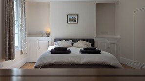 A bedroom with a bed, pillows, a bedside table, a lamp, and a framed picture on the wall. - Spacious three bedroom house with garden, close to O2, quick to central London (London)