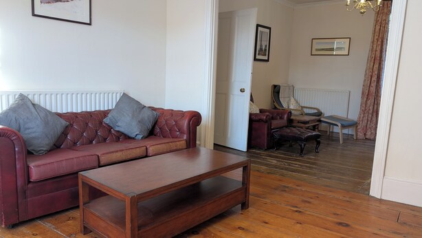 A living room with a leather sofa, a wooden coffee table, and a door leading to another room. - Spacious three bedroom house with garden, close to O2, quick to central London (London)