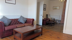 A living room with a leather sofa, a wooden coffee table, and a door leading to another room. - Spacious three bedroom house with garden, close to O2, quick to central London (London)