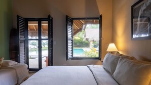 A bedroom with two beds, a window with a view of a pool and outdoor area, and a lamp on the nightstand. - Beachfront Paradise  Pool & Staff  (Sosúa)