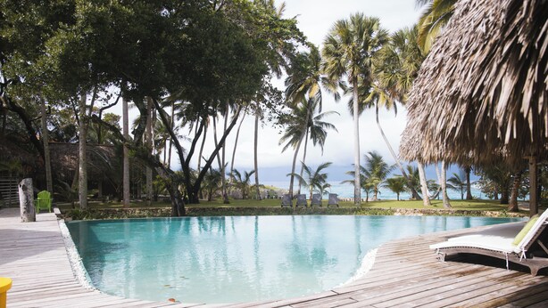 A wooden deck with a pool, lounge chairs, and palm trees. - Beachfront Paradise  Pool & Staff  (Sosúa)
