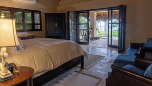 A bedroom with a bed, a desk, a chair, a wardrobe, and a view of the outdoors through a glass door. - Beachfront Paradise  Pool & Staff  (Sosúa)