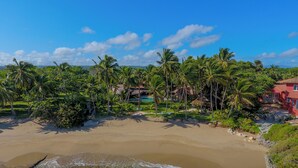 A beach with clear turquoise water, palm trees, and a red building. - Beachfront Paradise  Pool & Staff  (Sosúa)