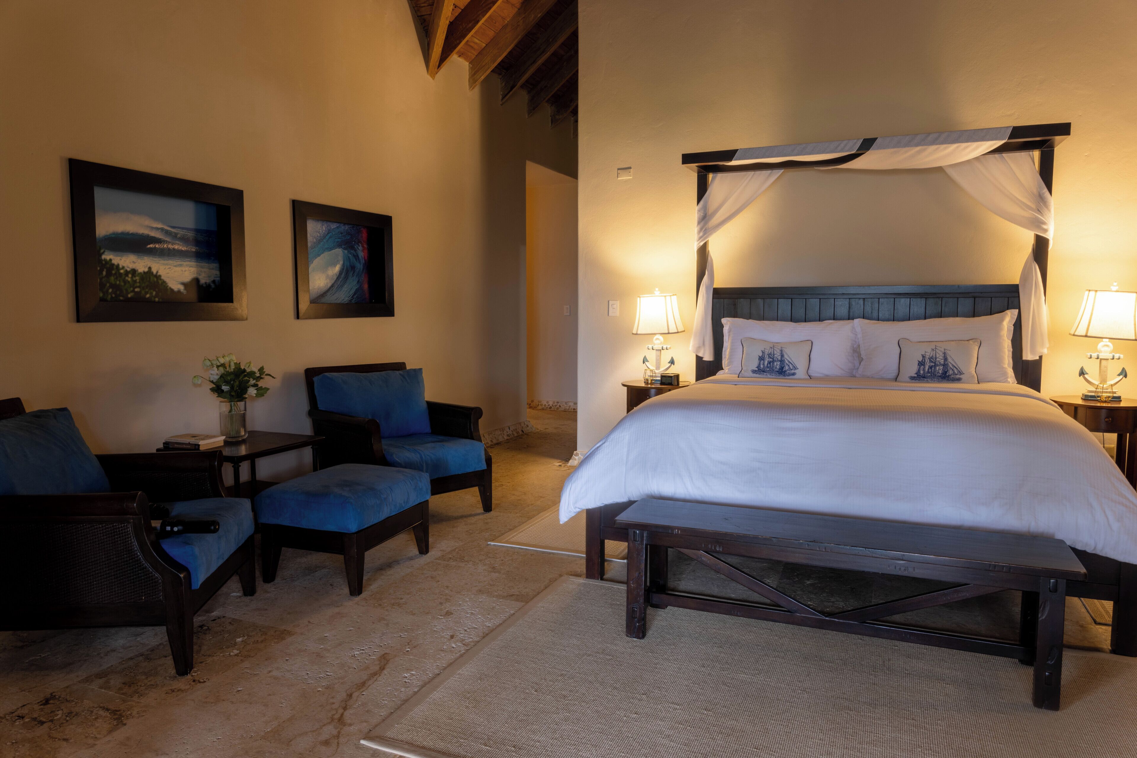 Habitación de hotel con una cama grande, dos sillones, un banco y dos mesitas de noche con lámparas.