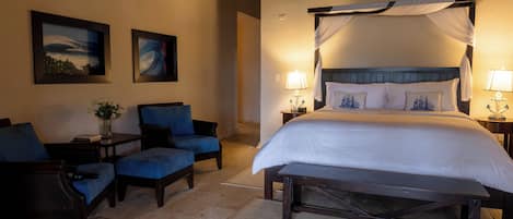 A hotel room with a large bed, two armchairs, a bench, and two bedside tables with lamps.