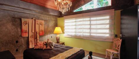 A bedroom with a bed, a chandelier, a window with blinds, a chair, and a lamp.