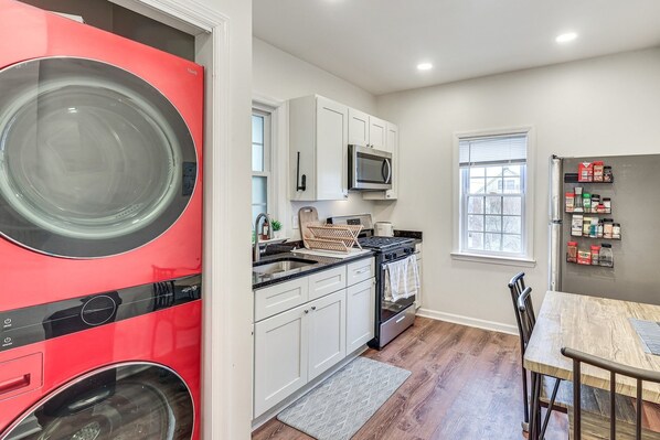 A compact kitchen with a red washing machine, white cabinets, a microwave, and a window with blinds. - Cozy 2-bedroom house in tranquil Belleville with AC (Belleville)