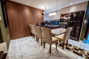 A modern kitchen with a dining area, featuring a marble-tiled floor, wooden panel wall, and contemporary appliances. - Apartment with Pool, Gym and BBQ Area (João Pessoa)