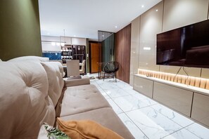 A modern living room with a sofa, a TV mounted on the wall, and a kitchen area in the background. - Apartment with Pool, Gym and BBQ Area (João Pessoa)