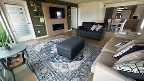 Una sala de estar con un sofá gris, un reposapiés y una alfombra estampada.