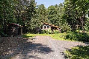 A rustic cabin with a gravel driveway, surrounded by dense forest.