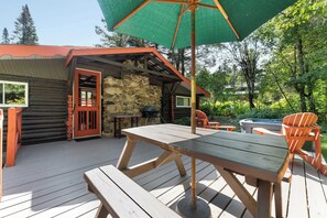 A wooden deck with a picnic table and chairs, a stone wall, and a red door.