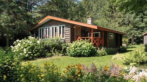 Una cabana amb un porxo, envoltada d'un jardí ple de plantes i flors diverses.
