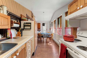 A kitchen with wooden cabinets, a dining table with chairs, a stove, and a red pot on it.
