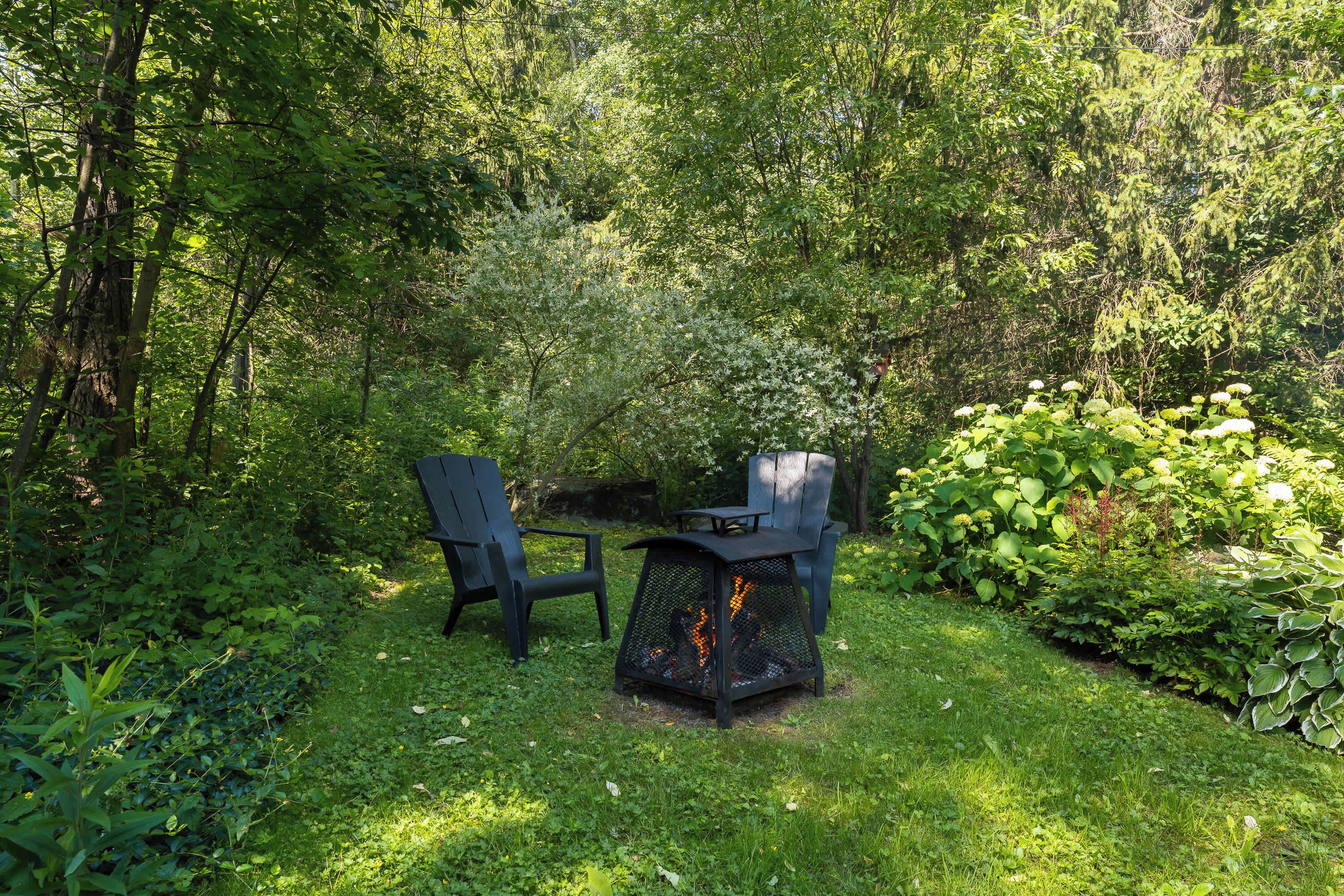 Un jardin agrémenté d’un foyer, de deux chaises et d’une végétation luxuriante.