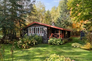 A cabin with a stone chimney, surrounded by lush greenery and a well-maintained garden.