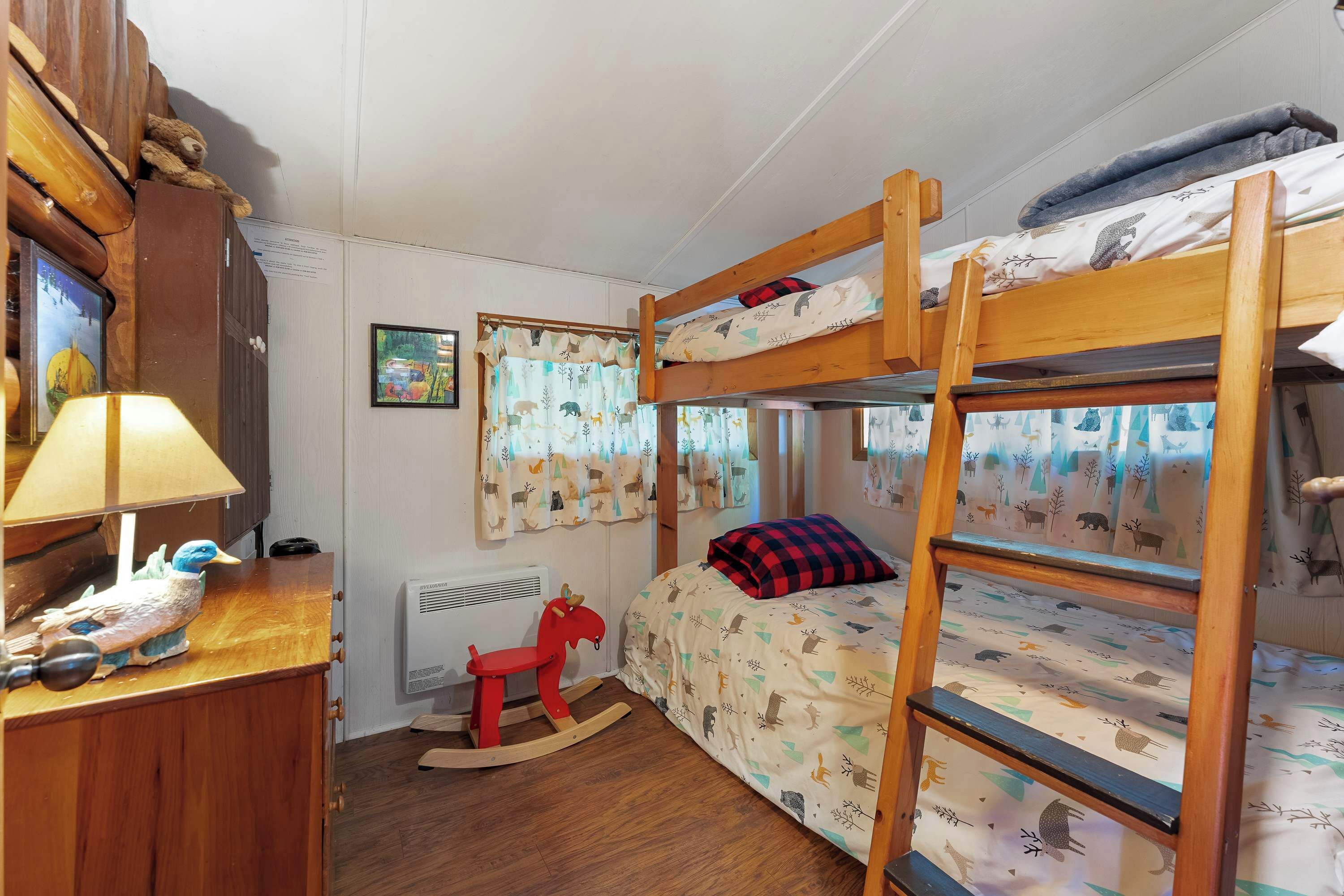 Une chambre pour enfant avec un lit superposé, un cheval à bascule, un bureau avec une lampe et une fenêtre avec des rideaux.