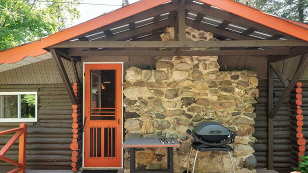 Una cabana de fusta amb paret de pedra, una porta de fusta i una graella al porxo.