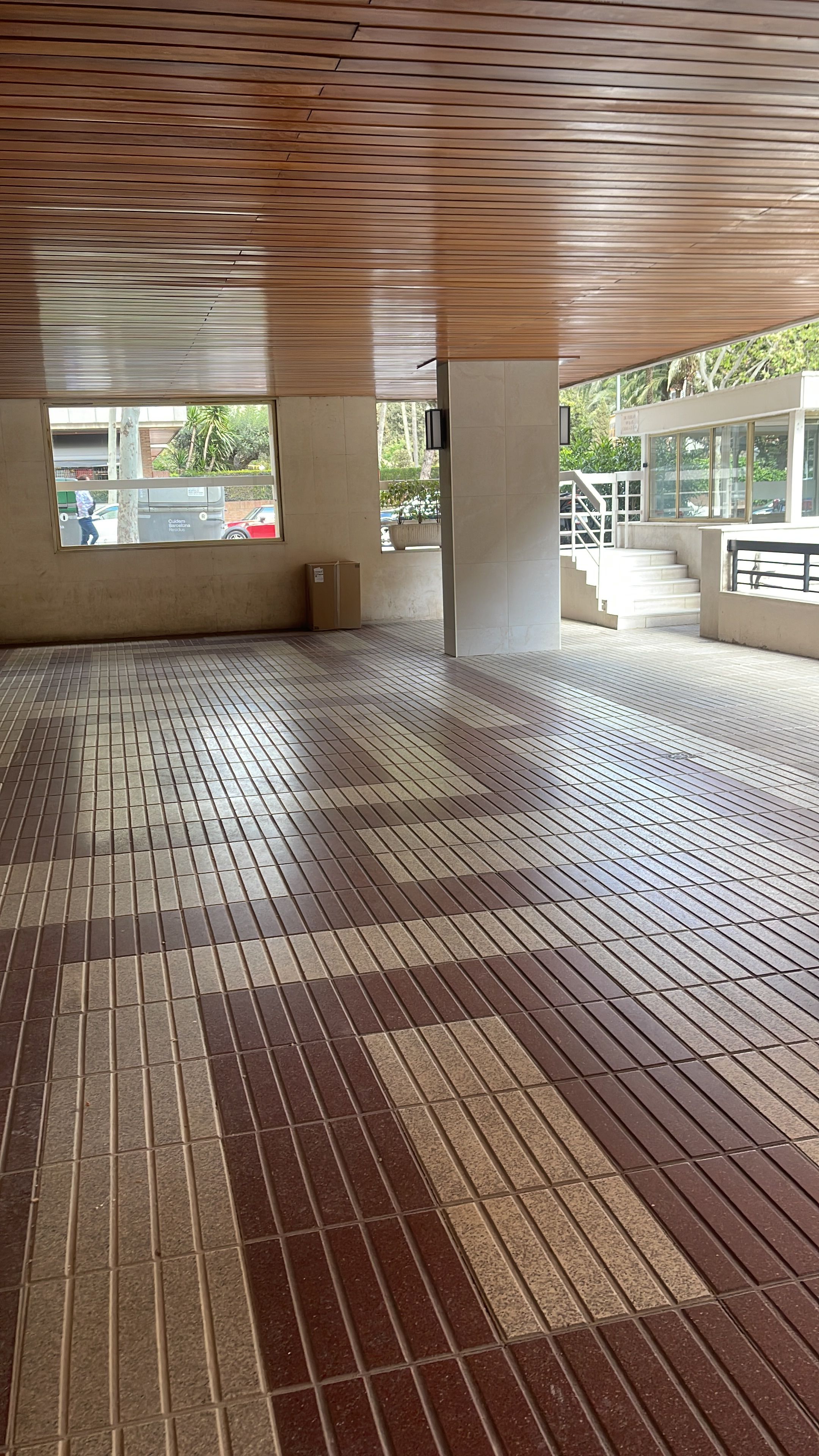 An indoor area with a tiled floor, a wooden ceiling, and a view of the outside through a window.