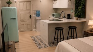 A compact living space with a kitchenette, a bed, a small bar area, and a door leading to another room. - Yamila (Barcelona)