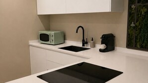 A modern kitchen with a white countertop, a black sink, a green microwave, and a coffee machine. - Yamila (Barcelona)