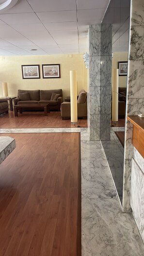 A lobby with a wooden floor, a marble column, a sofa, and framed artwork on the wall. - Yamila (Barcelona)