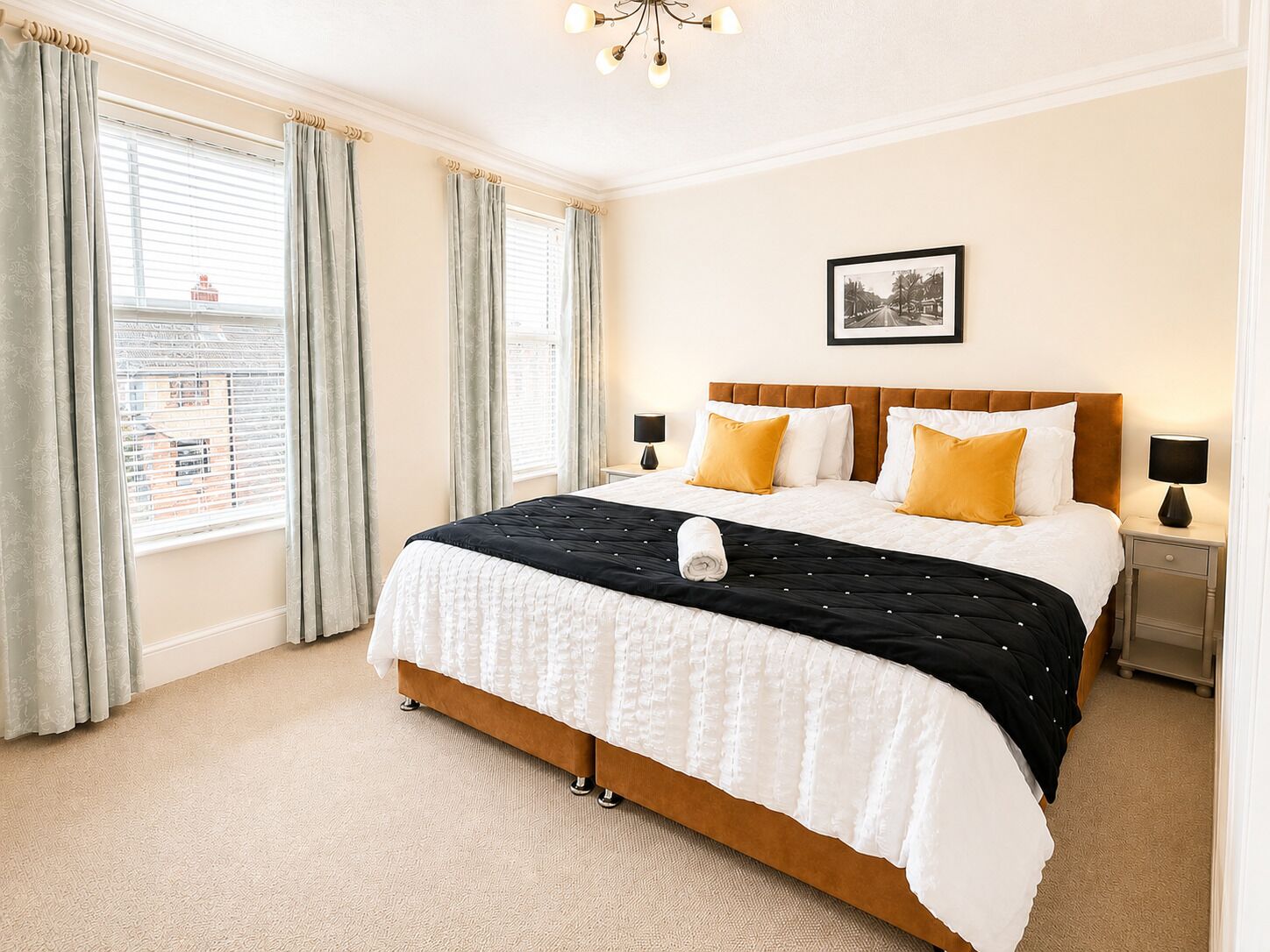 A hotel room with a large bed, two bedside tables, a chandelier, and a framed picture on the wall.
