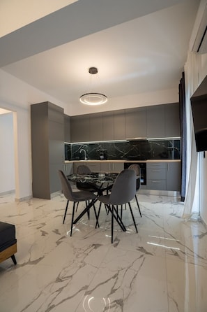A modern kitchen with a marble countertop, a dining table with chairs, and a built-in oven. - Brand New Spacious 3BR Apartment (Athens)