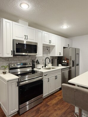 A modern kitchen with white cabinets, stainless steel appliances, a double sink, and a bar area. - Cozy Two-Level Basement Suite - Kitchen & Laundry (Orem)