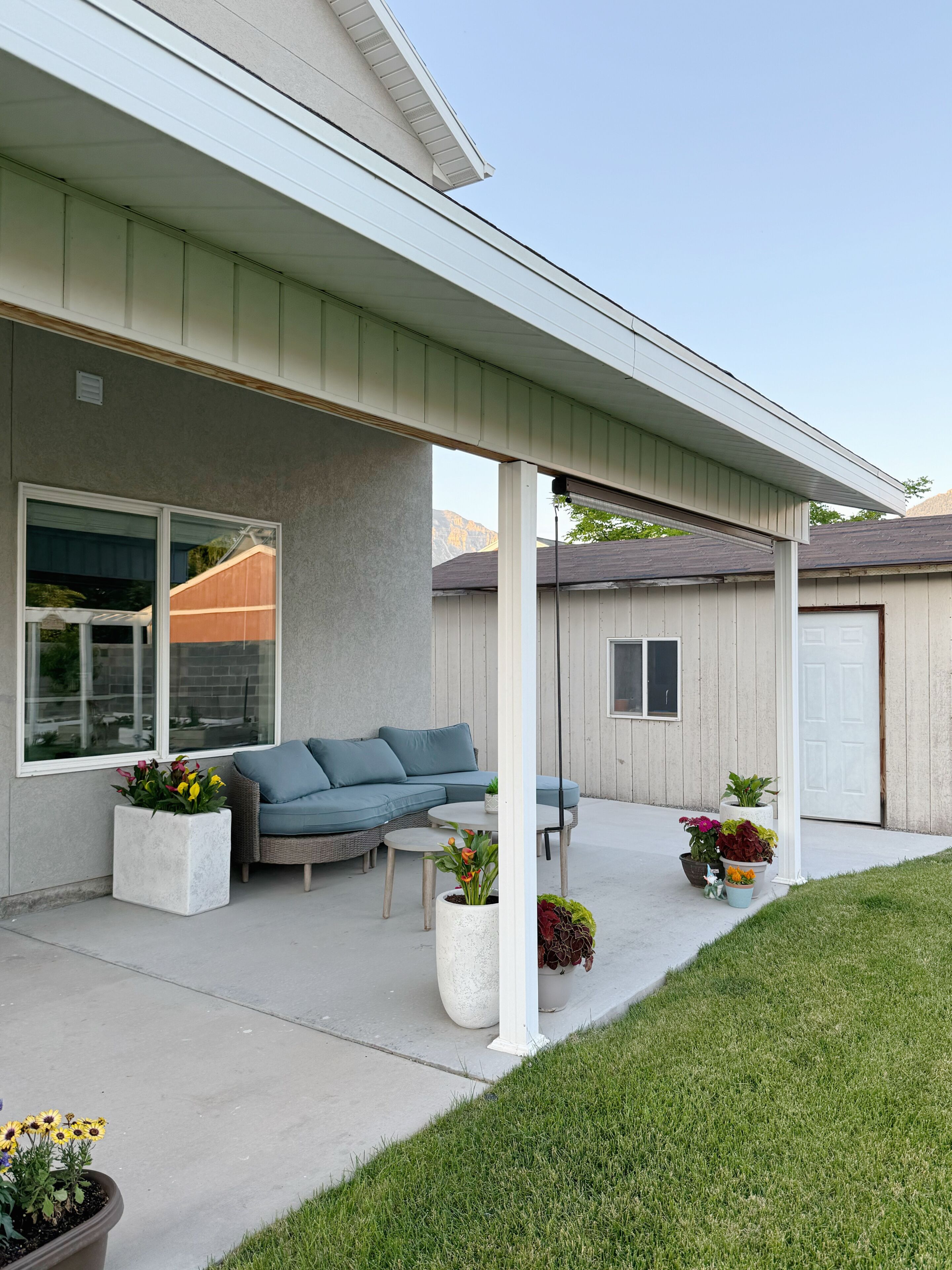 A covered patio area with a sofa, a table, and potted plants.