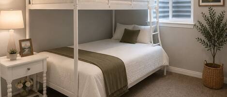 A bunk bed room with a window, a bedside table with a lamp, and a framed picture.