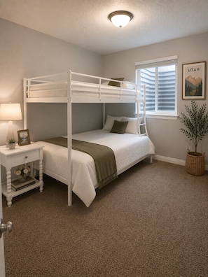 A bunk bed room with a window, a bedside table with a lamp, and a framed picture. - Cozy Two-Level Basement Suite - Kitchen & Laundry (Orem)