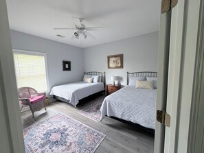 Ein Schlafzimmer mit zwei Betten, einem Deckenventilator, einem Fenster mit Jalousien, einem Sessel und einem Teppich.