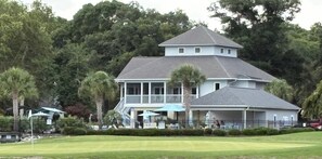 A two-story house with a balcony, surrounded by a fence and trees. - Spacious 2BR Ground Floor Retreat at Sea Trail • Golf • Beach • Pools (Sunset Beach)