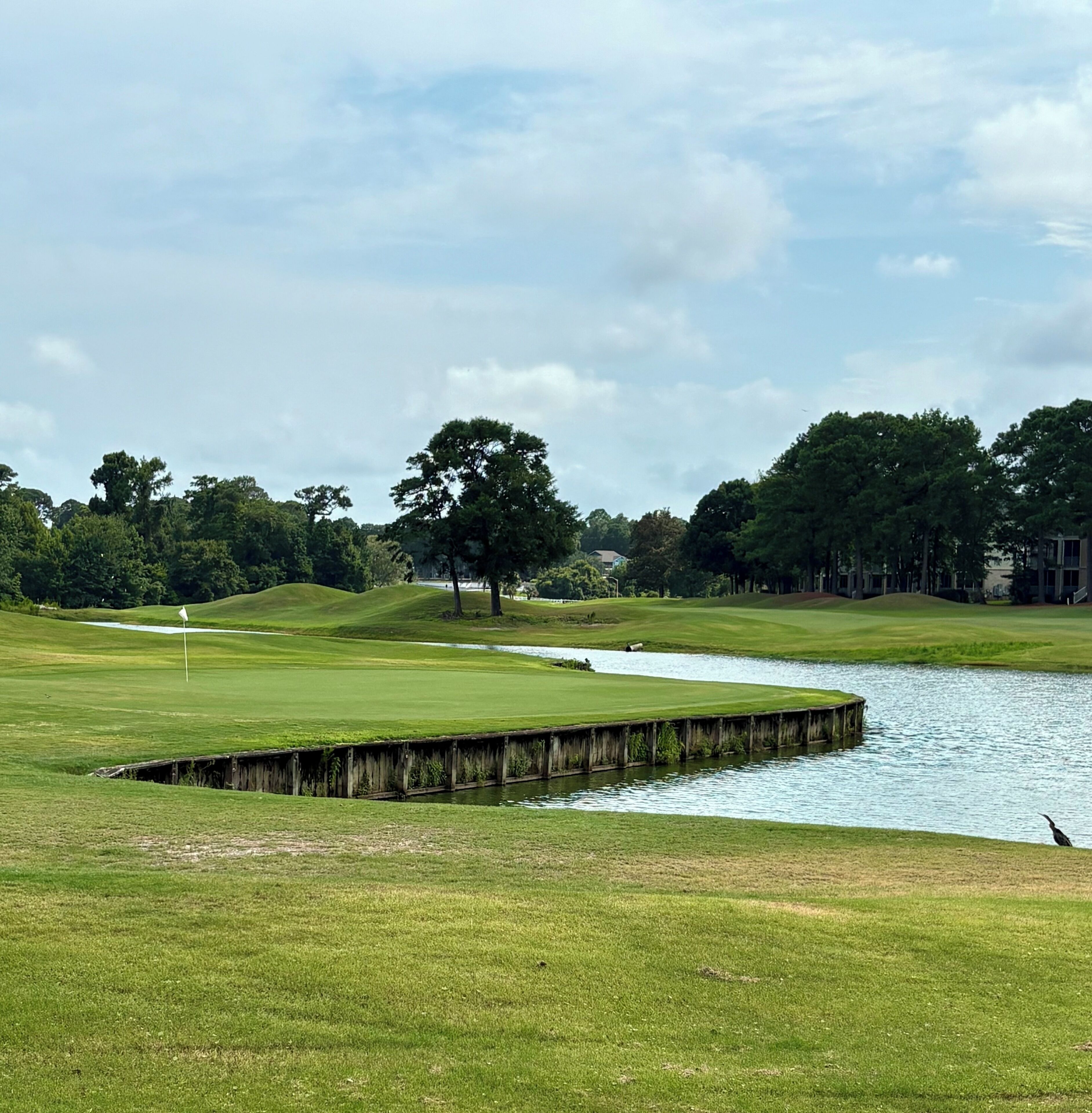 A golf course with a water hazard, a wooden bridge, and a flag.