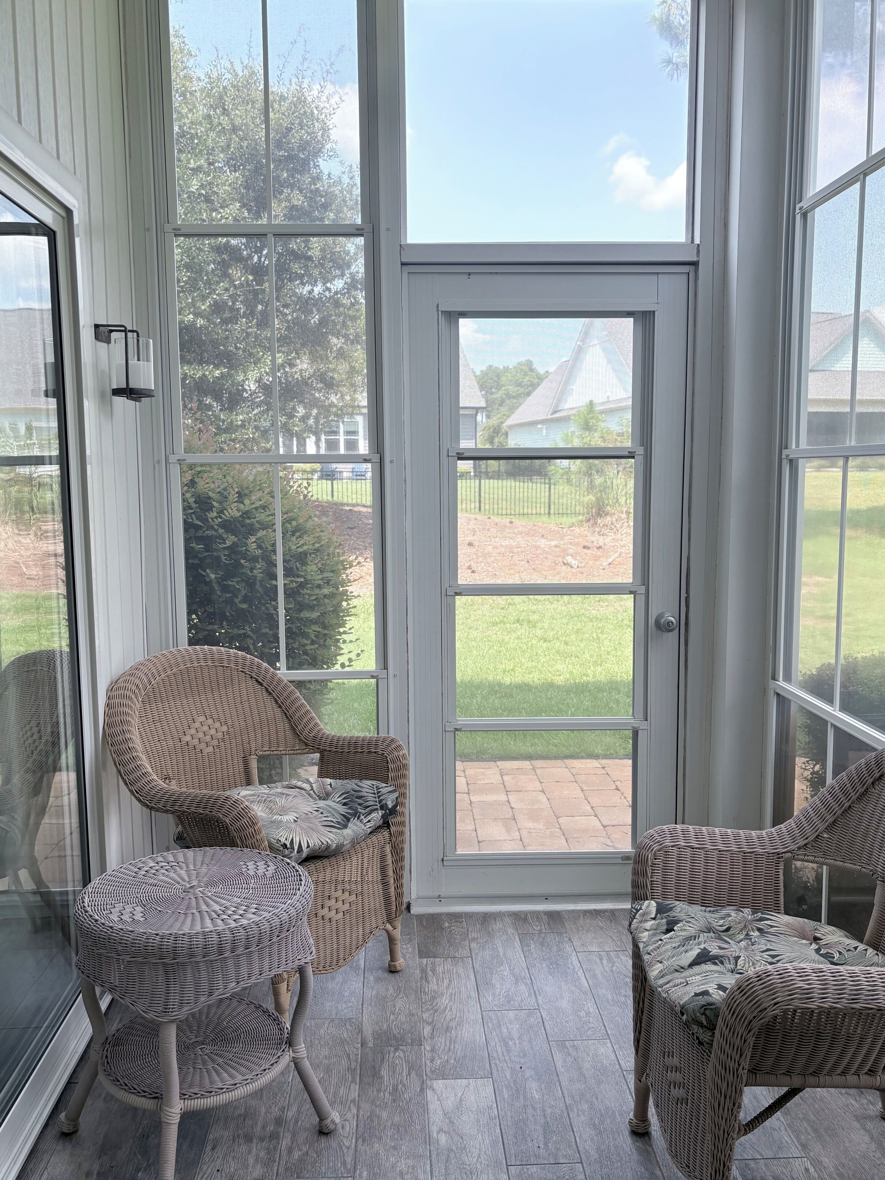 A covered patio area with wicker furniture and a glass door leading to a grassy yard.
