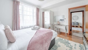 Ein Schlafzimmer mit einem Bett, einem Schreibtisch, einem Spiegel und einer Tür zu einem anderen Raum.