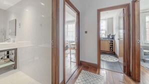 Ein modernes Badezimmer mit Waschtisch, einer Duschkabine und Blick in das Wohnzimmer durch eine offene Tür.