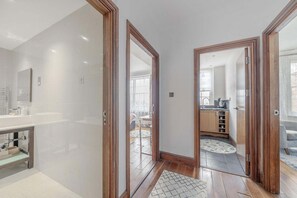 A modern bathroom with a vanity, a shower area, and a view into the living room through an open door. - Fantastic 1 Bedroom Apartment Just Off Marble Arch (London)