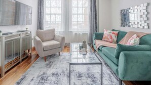 Ein Wohnzimmer mit Sofa, Sessel, Couchtisch und Fernseher an der Wand.