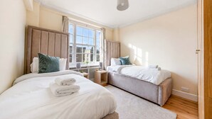 A hotel room with two beds, a window, a ceiling light, and a wooden floor. - Beautiful 2 Bedroom off Marble Arch (London)