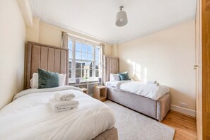 A hotel room with two beds, a window, a ceiling light, and a wooden floor. - Beautiful 2 Bedroom off Marble Arch (London)