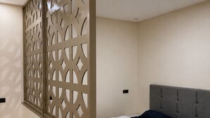 Un dormitorio con cama, cabecera tapizada en gris, suelo de madera y un separador decorativo con diseños geométricos.