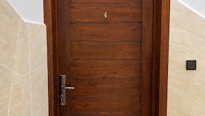 Una puerta de madera con el número 4, un picaporte y un objeto negro pequeño en la pared a la derecha.