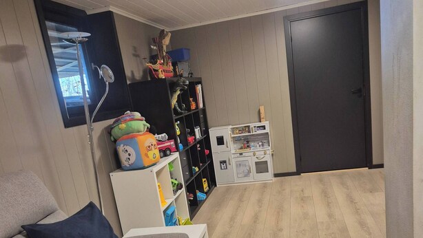 Una habitación con un sofá gris, un armario blanco, una puerta oscura y piso de madera.