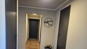 Un pasillo con suelo de madera, una lámpara en el techo, un reloj de pared y una planta en maceta.