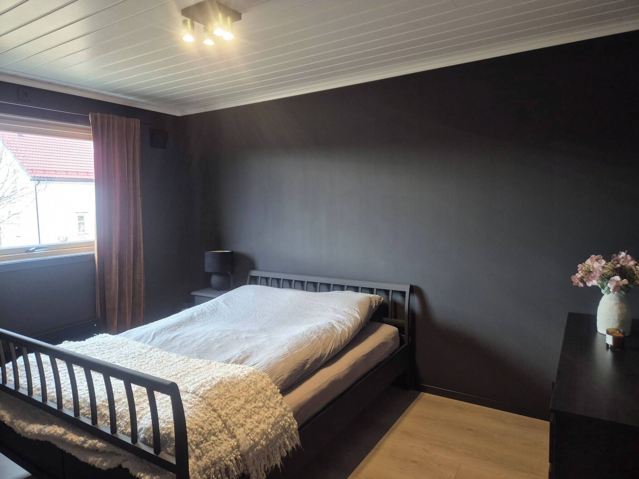 A bedroom with a bed, bedside table, lamp, and a window with curtains.