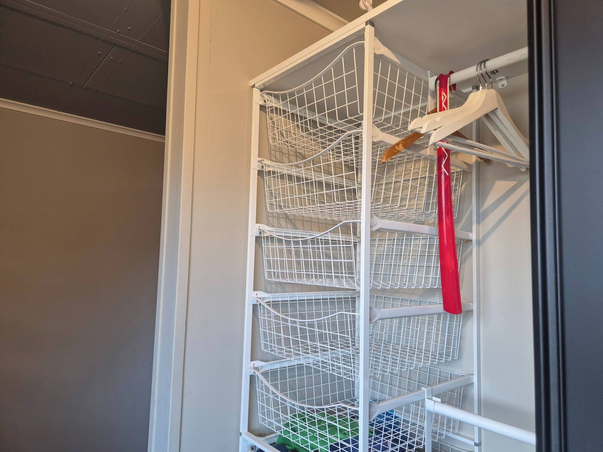 A white metal shelving unit with multiple wire baskets, a red hanger, and a wooden hanger.