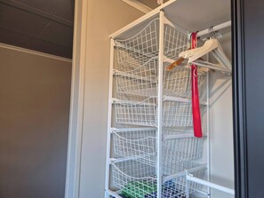 A white metal shelving unit with multiple wire baskets, a red hanger, and a wooden hanger.
